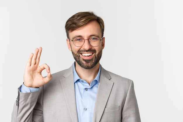 Nahaufnahme des hübschen bärtigen Mannes im grauen Anzug und in der Brille, empfehlen etwas