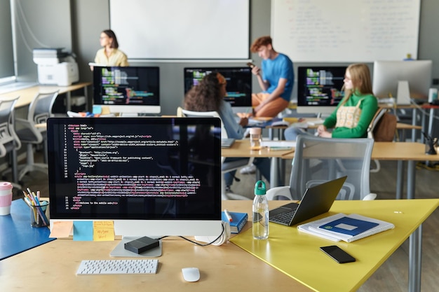 Nahaufnahme des Klassenzimmers mit Computer auf dem Schreibtisch im IT-Unterricht mit Schülern im Hintergrund