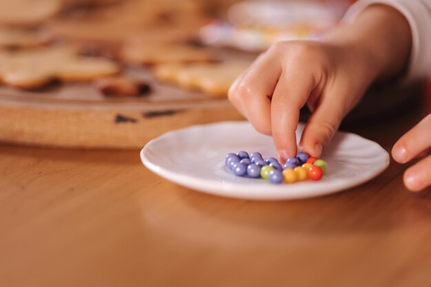 Nahaufnahme des kleinen Mädchens in Weihnachtsmütze schmückt Lebkuchen mit bunten Perlen Weihnachten und neu