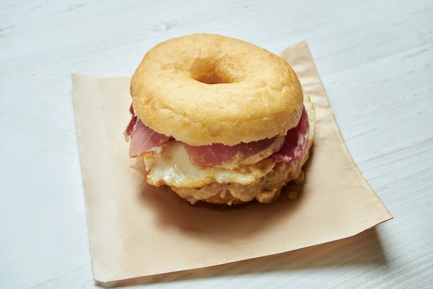 Nahaufnahme des leckeren Bagels mit Speck und Spiegelei auf einem Holztisch. Ungewöhnliches Donut-Sandwich. Frühstück