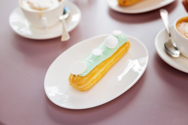 Nahaufnahme des leckeren leckeren Eclairs, der auf Teller dient, der auf rosa Oberfläche bleibt