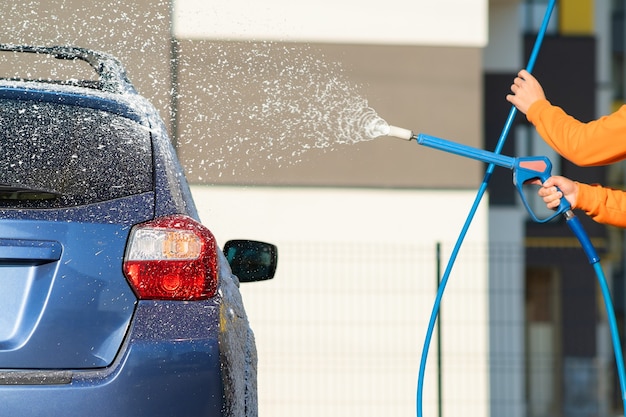 Nahaufnahme des männlichen Fahrers, der sein Auto mit kontaktlosem Hochdruckwasserstrahl in der Selbstbedienungs-Autowäsche wäscht.