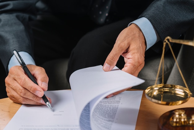 Nahaufnahme des männlichen Rechtsanwalts das Vertragsdokument auf dem Schreibtisch unterzeichnend