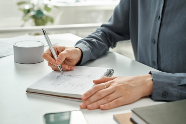 Nahaufnahme des Managers, der während der Arbeit im Büro Finanzstrategie in Notizblock schreibt