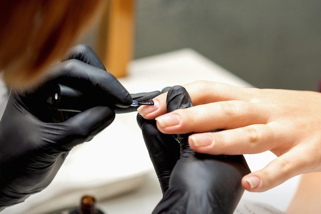 Nahaufnahme des Maniküre-Meisters, der Nägel mit dem transparenten Lack der weiblichen Nägel in einem Nagelstudio bedeckt