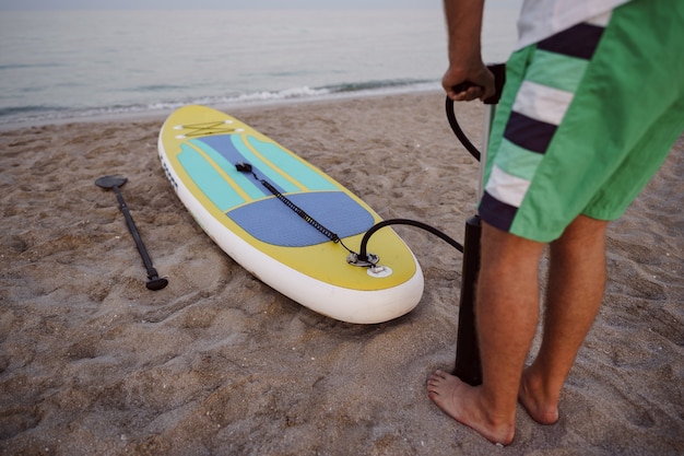 Nahaufnahme des Mannes bereitet sich auf das Paddeln auf einem Strand vor, der Sup-Board aufbläst?