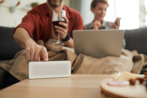 Nahaufnahme des Mannes, der das Radio auf dem Tisch einschaltet, während Wein mit Frau auf dem Sofa trinkt