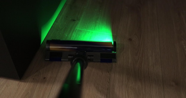 Nahaufnahme des Mannes Staubsauger mit einem modernen Staubsauger mit grüner Beleuchtung Reinigung des Hauses mit drahtlosen Staubsaugern Intelligente Reinigungstechnologie
