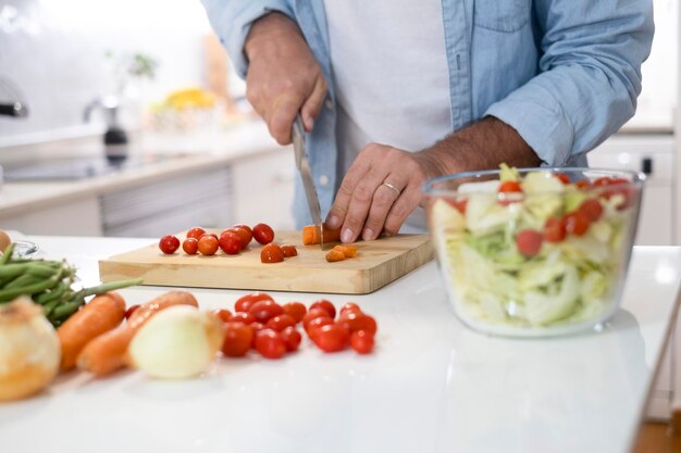 Nahaufnahme des Mannes zu Hause, der Gemüsesalat zum Mittagessen zubereitet Menschen in der Küche kochen und gesunde Ernährung genießen Ein nicht erkennbarer Mann, der Tomatenkirsche schneidet, um alleine zu essen