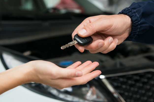 Nahaufnahme des Mechanikers, der dem Kunden in der Garage einen Autoschlüssel gibt