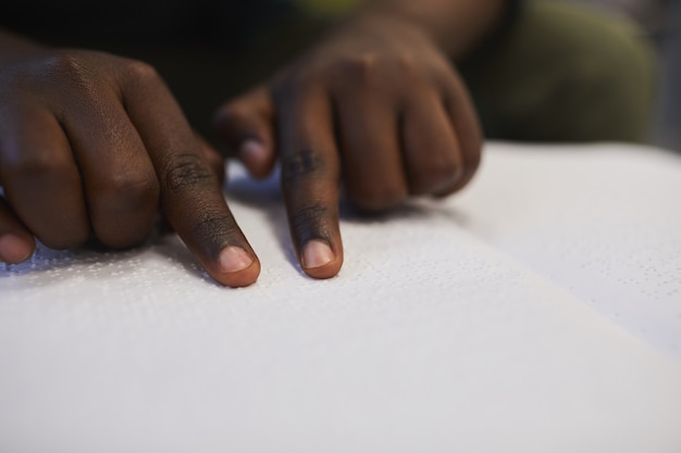 Nahaufnahme des nicht erkennbaren blinden afrikanischen Mannes, der Braillebuch liest, während in der Schule studiert