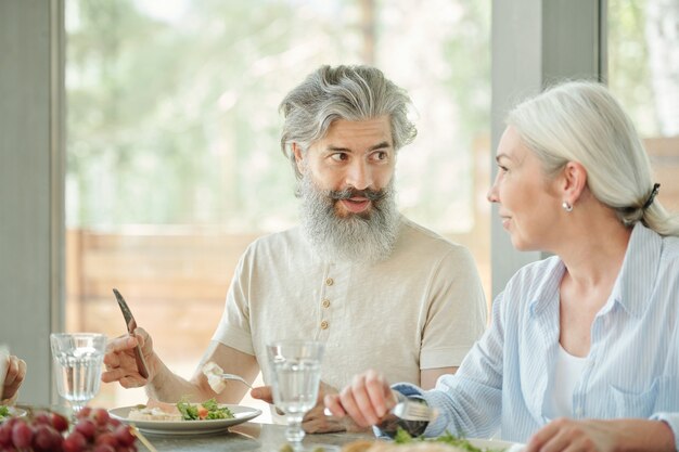 Nahaufnahme des nicht erkennbaren Mannes, der am Tisch sitzt und erfrischenden Salat mit Gabel und Messer isst