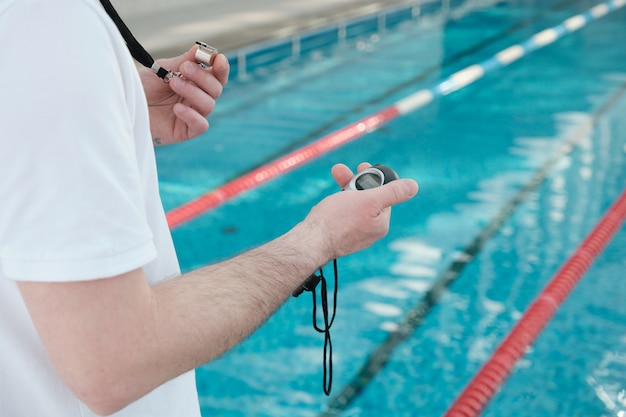 Nahaufnahme des nicht erkennbaren Trainers, der Pfeife hält und Stoppuhr beim Schwimmtraining verwendet