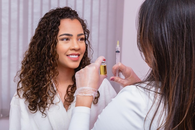 Nahaufnahme des Patienten, der Krankenschwester mit Spritze und Hyaluronsäure in der Hand beobachtet, um kosmetisches Verfahren durchzuführen. Kosmetikerin hält Botox in der Hand und zeigt den Patienten