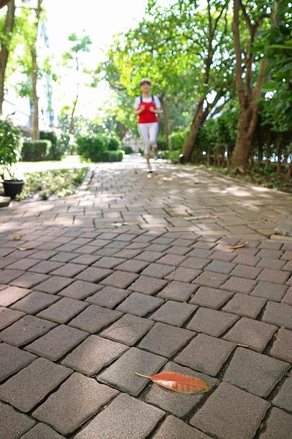 Nahaufnahme des Pflasterwegs im Park mit verschwommener Joggingfrau in der Ferne