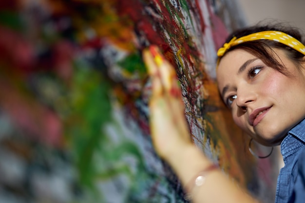 Nahaufnahme des Porträts einer entspannten jungen Malerin, die mit den Fingern Farbe auf die Leinwand aufträgt, während