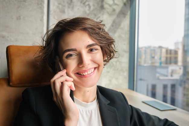 Nahaufnahme des Porträts einer Geschäftsfrau, die im Büro lacht und lächelt und am Telefon spricht