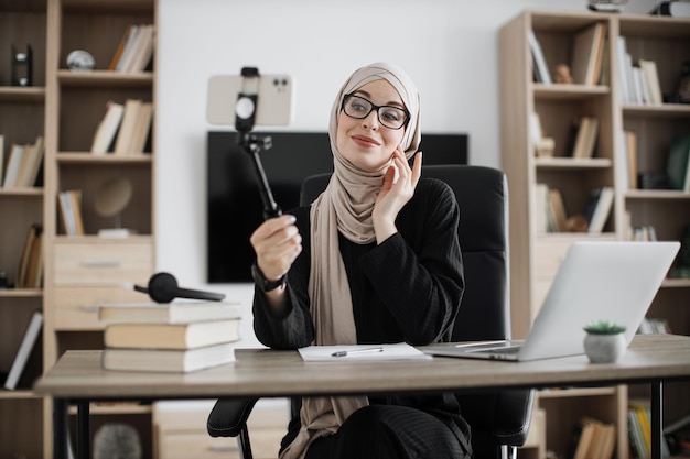 Nahaufnahme des Porträts einer jungen muslimischen Frau im Hijab, die mit einem Stock ein Selfie auf ihrem Smartphone macht