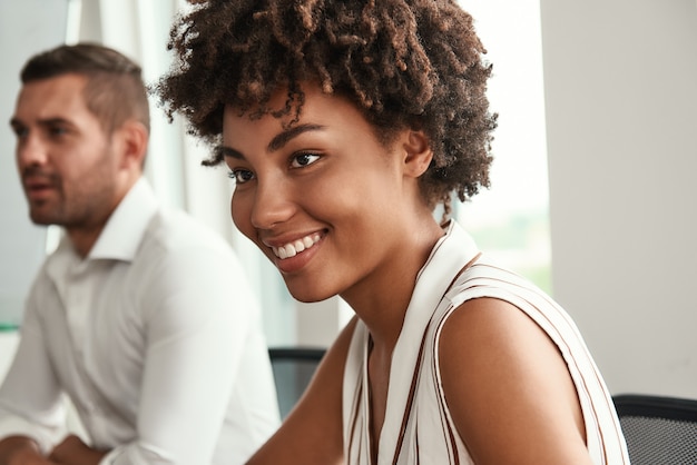 Nahaufnahme des Porträts einer jungen und schönen afroamerikanischen Frau, die bei einem Geschäftstreffen im modernen Büro sitzt. Brainstorming