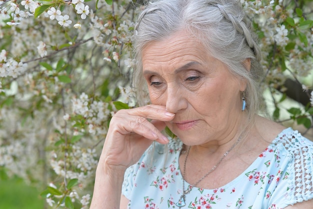 Nahaufnahme des Porträts einer traurigen Seniorin in der Nähe eines blühenden Frühlingsbaums