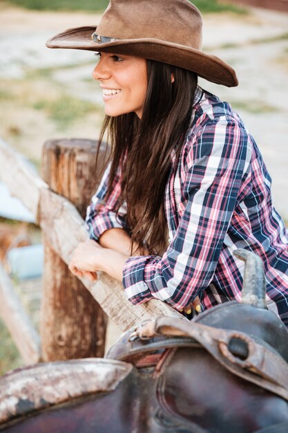 Nahaufnahme des Porträts eines lächelnden, glücklichen Cowgirls, das sich auf den Zaun auf der Ranch stützt