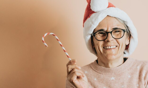 Nahaufnahme des Porträts senior alte weiße Haare Frau mit Weihnachtsmann-Hut lächelnd in die Kamera spielen. Weihnachten feiern. steht vor einem pastellfarbenen Hintergrund.Weihnachtskleidung.Textfreiraum.Werbefläche