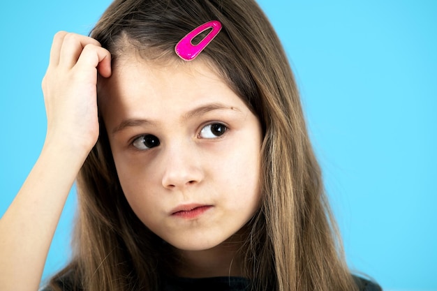 Nahaufnahme des Porträts von verärgerten und nachdenklichen kleinen Mädchen mit süßer rosa Haarnadel auf blauem Hintergrund.