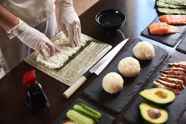 Nahaufnahme des Prozesses der Vorbereitung des rollenden Sushi. Nori und weißer Reis. Die Hände der Köche berühren Reis. Chefkoch beginnt Sushi zu kochen