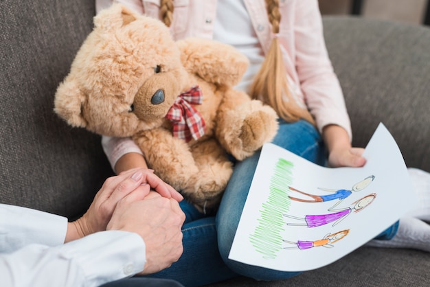 Foto nahaufnahme des psychologen hand eines mädchens halten zeichnungspapier mit gezogener familie halten