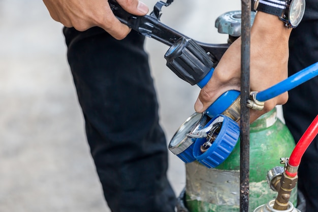 Nahaufnahme des Reparaturmanns der Klimaanlage Installieren Sie ein Manometer an den Brenngasen und am Sauerstofftank, um Metalle, Autogenschweißen und Autogenschneidverfahren zu schweißen oder zu schneiden