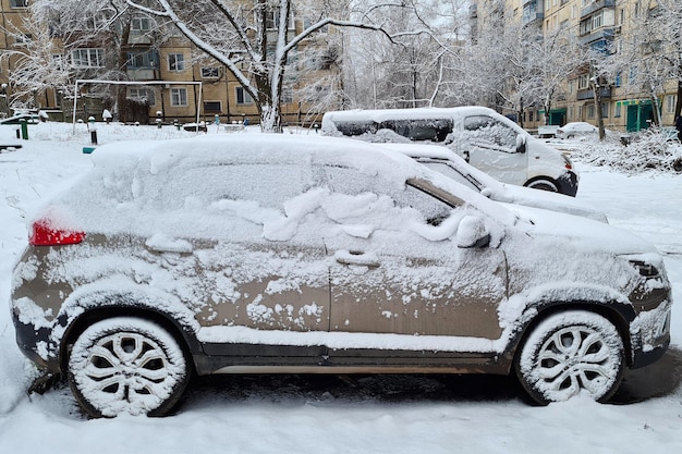 Nahaufnahme des schneebedeckten grauen SUV-Autos unter Schneesturm Kalter Winter frostig schneebedeckter Hintergrund