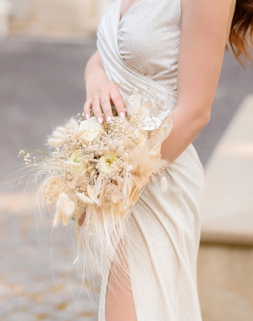 Nahaufnahme des schönen Blumenstraußes mit beigen Blumen, die elegantes Brautmädchen in minimalistischem Hochzeitskleid gekleidet halten Elegante Frau im hellen Stil Hochzeitskleid Zeremonie Hochzeitszubehör