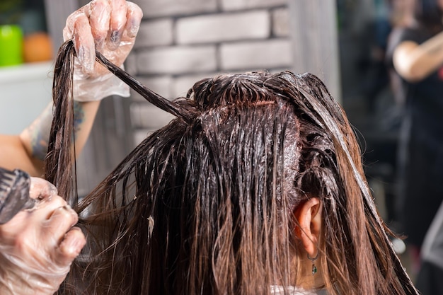 Nahaufnahme des Stylisten hält in der Hand brünette Haare und färbt mit Pinsel, während der Kunde im Schönheitssalon auf einem Stuhl sitzt