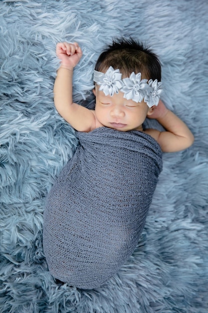 Nahaufnahme des süßen Neugeborenen mit Blumenstirnband auf grauen Wollteppichen, Modekonzept