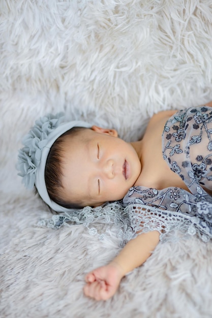 Nahaufnahme des süßen Neugeborenen mit Blumenstirnband auf weißen Wollteppichen, Modekonzept