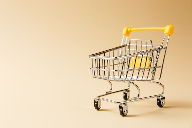 Nahaufnahme des Supermarkt-Einkaufswagens zum Einkaufen mit schwarzen Rädern und gelben Kunststoffelementen am Griff einzeln auf beigem Hintergrund. Konzept des Einkaufens. Kopieren Sie Platz für Werbung.