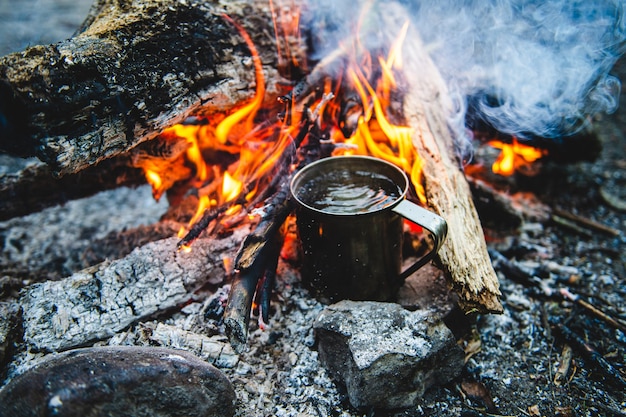 Nahaufnahme des Tees im Metallbecher erwärmt sich im Lagerfeuer