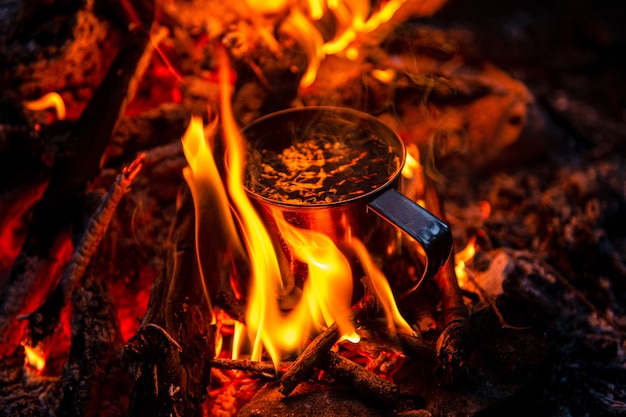 Nahaufnahme des Tees im Metallbecher erwärmt sich im Lagerfeuer