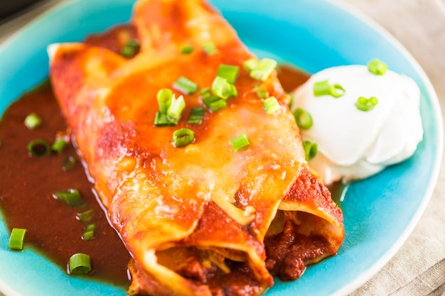 Nahaufnahme des Tellers mit Hühnchen-Enchiladas, garniert mit Frühlingszwiebeln und Sauerrahm.