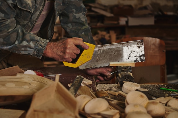 Nahaufnahme des Tischlers, der Holz mit einer Säge in seiner Werkstatt sägt, um handgefertigte Handwerksprodukte aus Holz herzustellen?