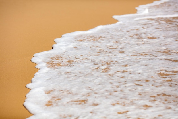 Nahaufnahme des tropischen Sandstrandes mit schäumenden Meereswellen