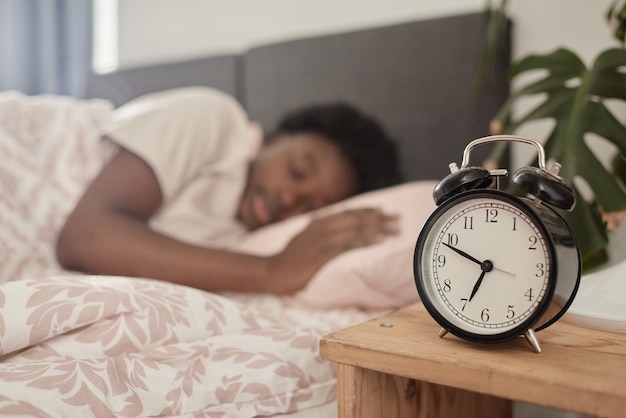 Nahaufnahme des Weckers, der auf dem Nachttisch steht, mit einer Frau, die im Hintergrund in ihrem Bett schläft