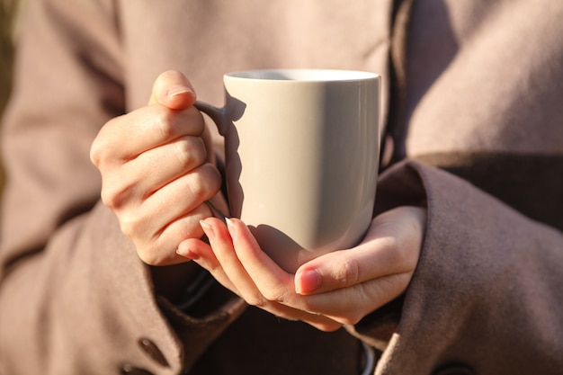 Nahaufnahme des Wegwerfbechers des Kaffees oder des Tees in der Hand der Frau. Herbstpark mit Bäumen und gelben Blättern