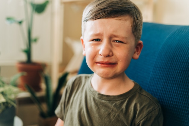 Nahaufnahme des weinenden kleinen Jungen, der zu Hause auf der Couch sitzt, verärgert das Kind