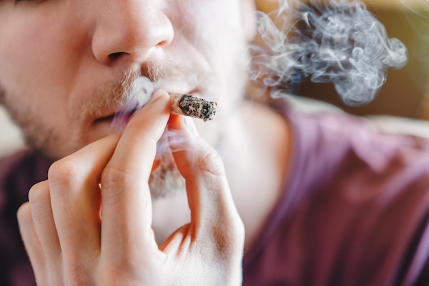 Nahaufnahme des zugeschnittenen Bildes eines jungen Mannes, der Marihuana oder Zigarette raucht