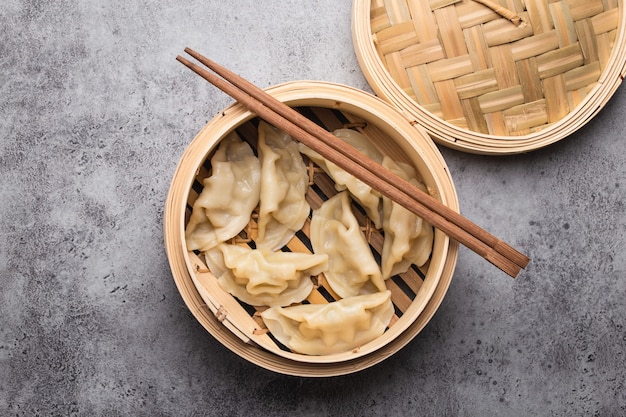 Nahaufnahme, Draufsicht auf traditionelle asiatische/chinesische Knödel im Bambusdampfer mit Stäbchen auf grauem rustikalem Steinhintergrund. Authentische chinesische Küche