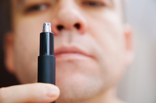 Nahaufnahme ein Mann schneidet sein Nasenhaar mit einem selektiven Fokus des Trimmers