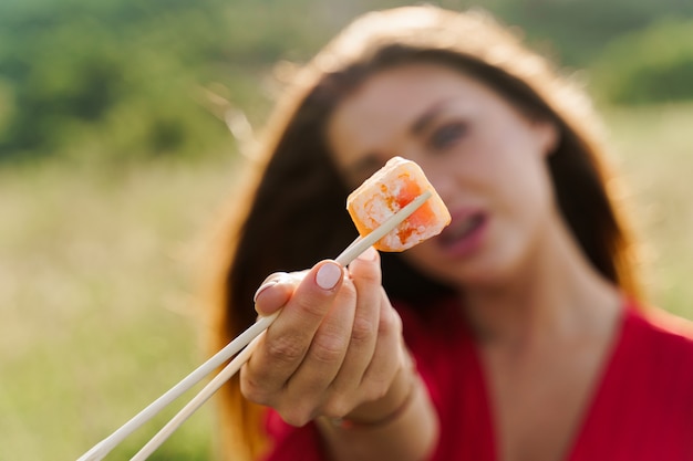 Nahaufnahme ein Sushi. Attraktives Mädchen hält Sushi mit Stäbchen in den Händen und gibt dir. Kurier lieferte Sushi-Set für hübsche Frau. Blackbox mit Sushi, Wasabi, Ingwer.