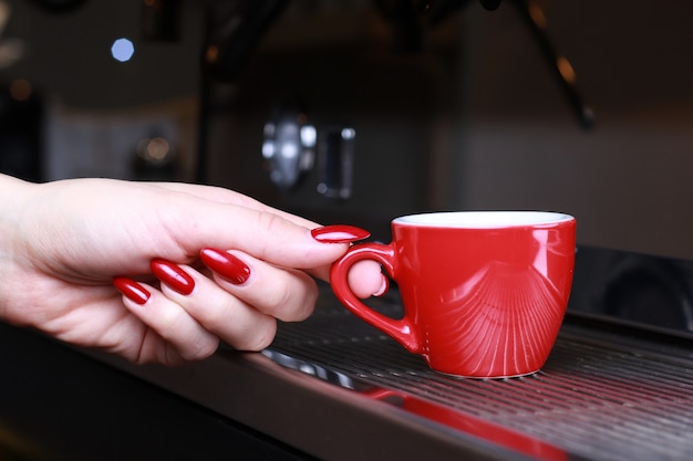 Nahaufnahme, eine Frauenhand, die eine Tasse Kaffeetassen hält, steht auf dem Grill in der Kaffeemaschine