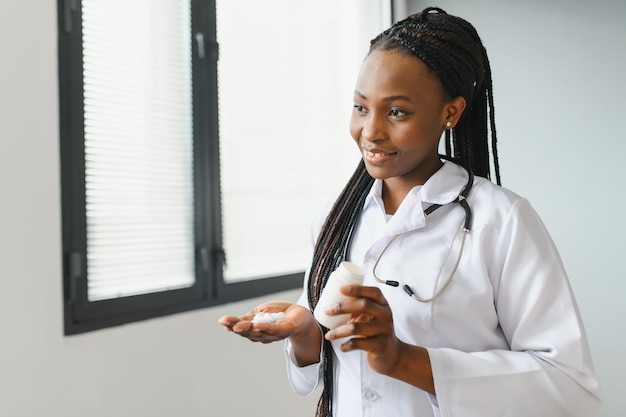 Nahaufnahme einer abgeschnittenen horizontalen Aufnahme einer lächelnden afrikanischen Ärztin oder Apothekerin, die bunte Blasen mit Pillen hält, die sie der Kamera zeigen, während sie in der Apotheke oder im Krankenhaus stehen